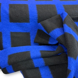 Könnte beinhalten: Nahaufnahme eines blau-schwarz karierten Stoffes. Der Stoff hat eine weiche Textur und ein sich wiederholendes Muster aus schwarzen Quadraten auf einem leuchtend blauen Hintergrund. Der Stoff ist gefaltet und zeigt Tiefe und Dimension.