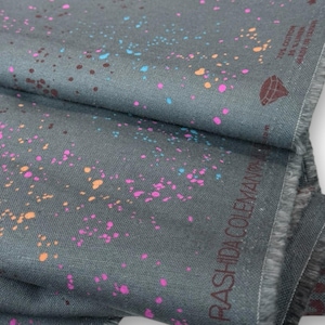Könnte beinhalten: Grauer Stoff mit farbenfrohem Farbspritzer-Design in Pink, Orange, Blau und Braun. Der Stoff ist gefaltet und zeigt die Textur und den Namen "RASHIDA COLEMAN" am Rand. Der Stoff besteht aus 70 % Baumwolle und 30 % Leinen.