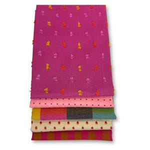 Könnte beinhalten: Ein Stapel bunter Stoffstücke. Das oberste Stück ist ein leuchtendes Fuchsia mit gestickten floralen Akzenten. Darunter befinden sich Stücke in Rosa, Gelb und Creme, jedes mit einzigartigen Mustern, darunter Punkte und Streifen. Die Stoffe sind ordentlich gefaltet.