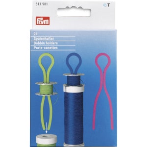 Könnte beinhalten: Eine Packung mit drei Prym Spulenhaltern. Die Halter sind aus flexiblem Kunststoff und in den Farben Grün, Blau und Pink erhältlich. Die Verpackung enthält den Text "21 Spulenhalter Bobbin holders Porte-canettes".