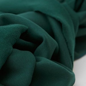 Puede incluir: Primer plano de una tela verde oscuro con una superficie suave y texturizada. La tela est&aacute; doblada y drapeada, mostrando su ca&iacute;da y textura.