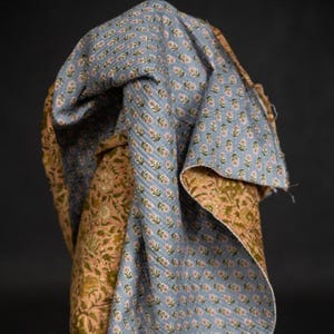 May include: A folded textile featuring a floral pattern in shades of blue, pink, and green. The fabric has a quilted texture and appears to be made of cotton. The design is repeated across the surface, creating a cohesive and visually appealing pattern.