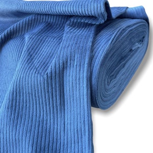 K&ouml;nnte beinhalten: Eine Rolle blauen Cordstoffes mit gerippter Struktur. Der Stoff ist gefaltet und aufgerollt, wodurch die Breite und die Struktur des Materials sichtbar werden.