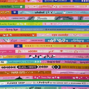 Könnte beinhalten: Ein mehrfarbiger Stoffdruck mit horizontalen Streifen, verschiedenen Texten und grafischen Symbolen. Das Muster enthält Beschriftungen wie 'whatnot', 'Florida', 'eye candy', 'Aviary', 'HEIRLOOM', 'ADORN', 'Snap to Grid', 'BLACK and WHITE' und 'FLOWER SHOP'.