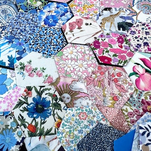 Könnte beinhalten: Eine Patchwork-Decke aus verschiedenen floralen und gemusterten Stoffen in Blautönen, Rosa und Weiß. Die Decke besteht aus sechseckigen Stücken, die zusammengenäht sind.