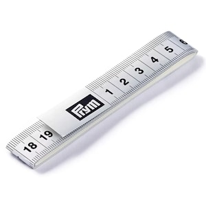 Könnte beinhalten: Ein weißes und schwarzes Prym-Maßband, das sowohl Zoll als auch Zentimeter anzeigt. Das Band ist gefaltet und zeigt Messungen von 1 bis 6 Zoll und 18 bis 19 Zoll an. Das Prym-Logo ist sichtbar.