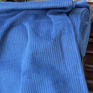 K&ouml;nnte beinhalten: Eine Rolle blauen Cordstoffes mit gerippter Struktur. Der Stoff ist in der Mitte gefaltet und die Rolle ist im Hintergrund sichtbar.