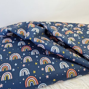 Könnte beinhalten: Dunkelblauer Stoff mit einem sich wiederholenden Muster aus bunten Regenbogen und weißen Sternen. Die Regenbogen haben Schichten aus Rosa, Gelb und Orange. Der Stoff ist gefaltet und zeigt die Textur und das Muster.