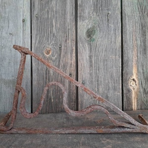 May include: A rusty metal bracket with a decorative, curved design. The bracket is made of iron and has a dark brown patina. It is likely an antique or vintage piece.