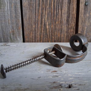 以下が含まれることがあります： バネ機構を備えたヴィンテージの金属製コルクスクリュー。コルクスクリューは、円形のハンドルと、バネと平らな丸い端を備えた長方形のフレームを備えています。金属は素朴で古びた外観で、摩耗や錆の兆候が見られます。