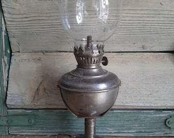 May include: A silver oil lamp with a clear glass globe. The lamp has a round base and a decorative metal top.