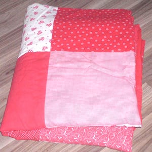 Könnte beinhalten: Rote und weiße Patchwork-Decke mit verschiedenen Mustern, darunter Herzen, Punkte und Blumenmuster.