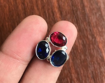 May include: A silver ring with three oval-shaped gemstones. The center stone is red, and the two outer stones are blue.