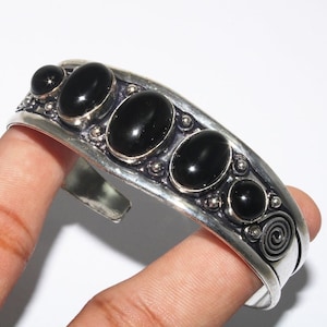 Op de afbeelding: Zilveren armband met vijf zwarte ovale edelstenen ingelegd in een decoratief zilveren ontwerp.