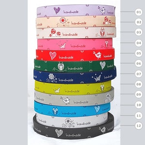 Könnte beinhalten: Ein Stapel bunter Bänder mit dem Aufdruck "handmade". Jedes Band hat ein anderes Muster, darunter Herzen, Blumen, Kronen und Vögel. Die Bänder sind in verschiedenen Farben erhältlich, wie z. B. Lila, Beige, Rosa, Rot, Grün, Blau, Gelb, Grau und Schwarz.