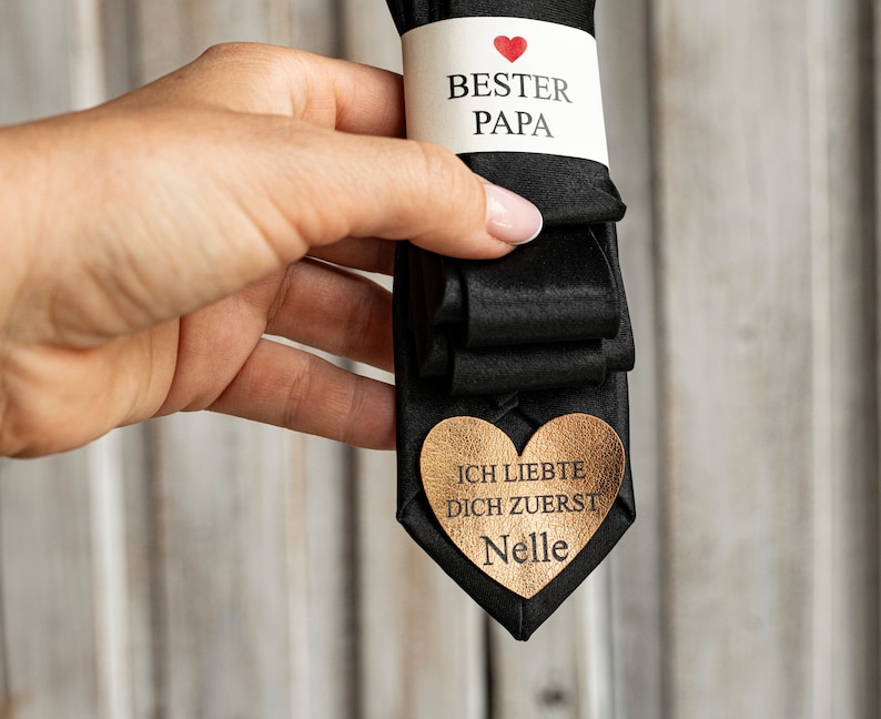 May include: Black tie with a white tag that says "Best Dad" with a red heart and a gold heart-shaped tag that says "I loved you first, Nelle".