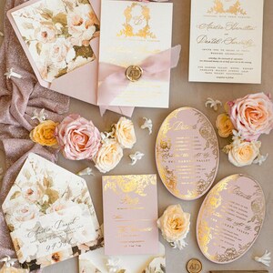 May include: Wedding invitation suite with a floral theme. The invitations are pink and gold with a floral design and the text "Anitia Daniel" and "Anitia Hamilton and Daniel Smith".