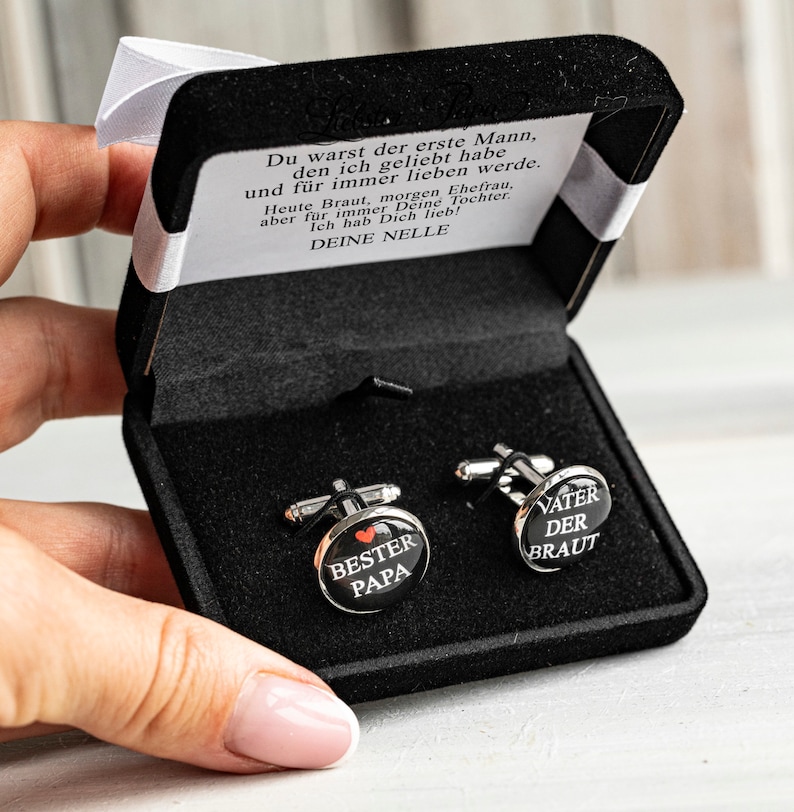 May include: A black velvet box with two silver cufflinks. One cufflink says "Best Papa" with a red heart. The other cufflink says "Father of the Bride".