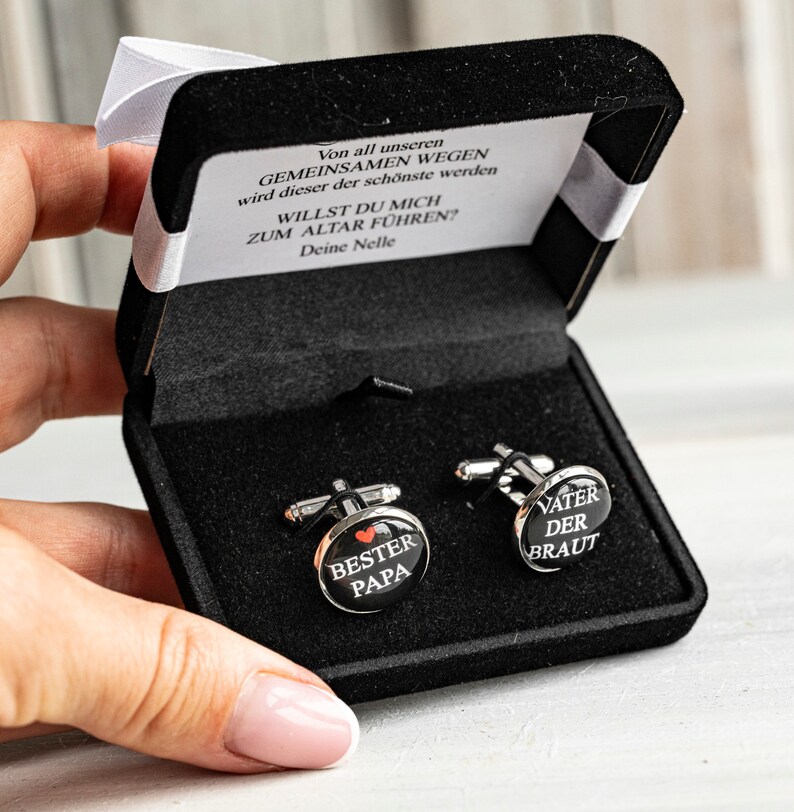 May include: A black velvet box with two silver cufflinks. One cufflink says "Best Dad" with a red heart and the other says "Father of the Bride".