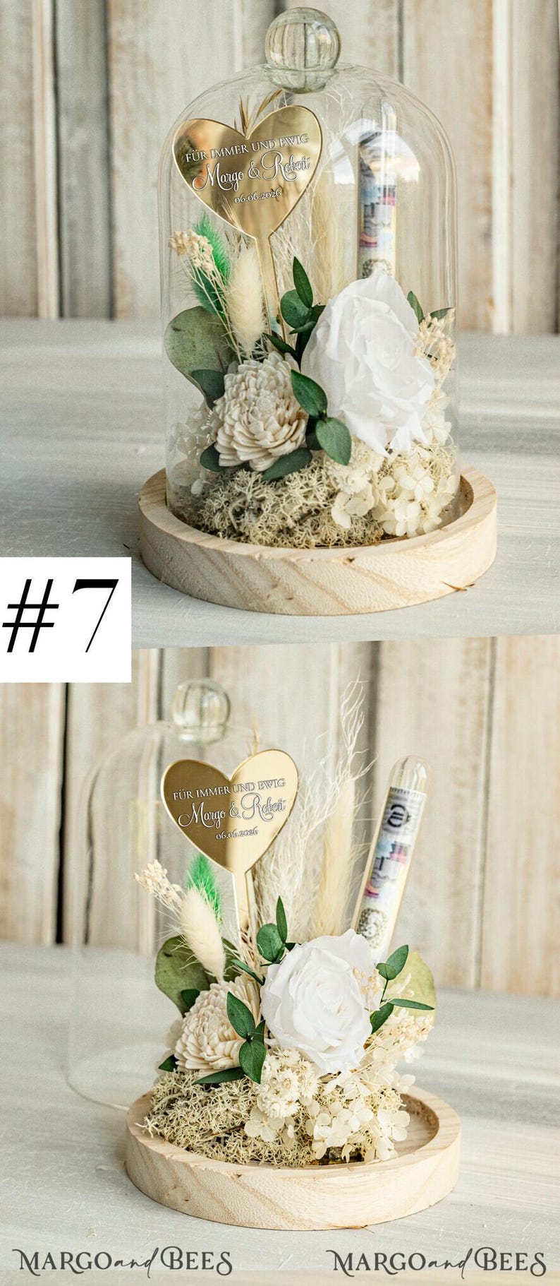 May include: A glass dome with a wooden base contains a white rose, dried flowers, and greenery. A gold heart-shaped plaque with the text "F&Uuml;R IMMER UND EWIG Margo & Robert 06.06.2020" is attached to a stem inside the dome.