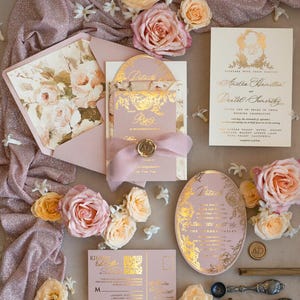 May include: A blush pink wedding invitation suite with gold foil accents and floral designs. The invitation features the couple's names, wedding date, and location. The RSVP card includes a QR code. The invitation is decorated with blush pink roses and a pink ribbon.