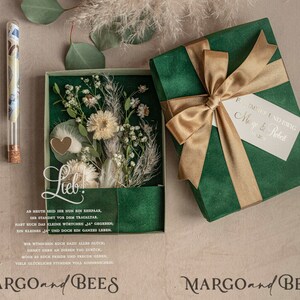 May include: A green box with a gold ribbon and a white tag that says "Forever and Ever Margo & Robert". The box is open and inside is a clear box with dried flowers and a small glass vial. The text "Lieb!" is written on the clear box. The text "MARGO and BEES" is written on the bottom of the image.