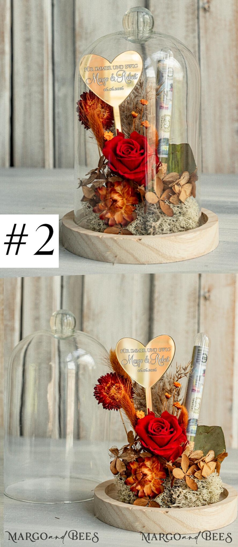 May include: A glass dome with a wooden base contains a preserved red rose and dried flowers. A gold heart-shaped plaque with the text "F&Uuml;R IMMER UND EWIG Margo & Robert 06.06.2016" is attached to a stick in the center of the dome.