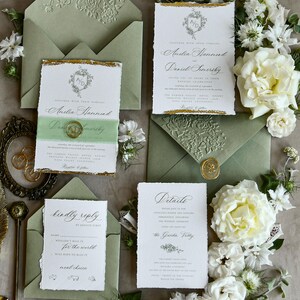 May include: A wedding stationery set featuring white paper cards with deckled edges, gold foil accents, and sage green envelopes with embossed floral patterns. The cards include text for Amelia Hammond and Daniel Somersby, a details card, and a reply card.