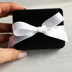 May include: A black velvet gift box with a white satin ribbon tied in a bow.