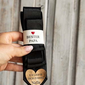 May include: Black satin tie with a white tag that says "Best Dad" with a red heart and a gold heart tag that says "I loved you first" with the name "Nelle" on it.