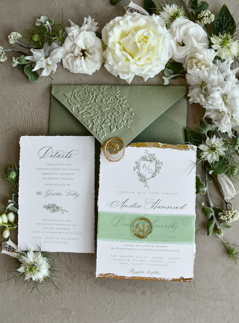 May include: A wedding invitation suite featuring a sage green envelope with a floral embossed flap, a white details card, and a main invitation with deckled edges, gold leaf accents, a green ribbon band, and gold wax seals with floral motifs.