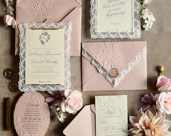 May include: A wedding stationery set featuring dusty pink envelopes with embossed floral patterns, cream-colored cards with white lace borders, gold-edged details, wax seals, and a small oval frame containing a portrait of a person.