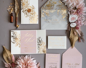 May include: Wedding invitation suite with a blush pink and gold color scheme. The invitation features a floral design with gold foil accents. The envelope is lined with a gray and gold floral pattern. The text on the invitation reads "Ashley & Mark".