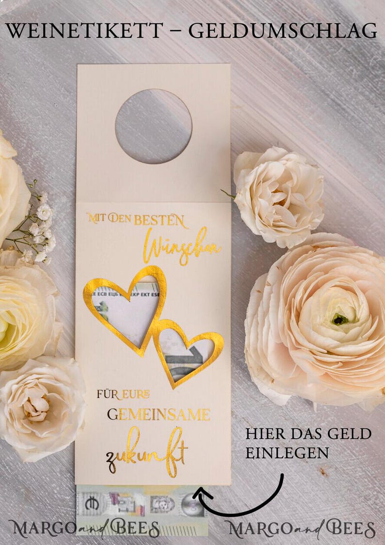 May include: A white card with gold lettering that says "WEINETIKETT - GELDUMSCHLAG" and "MIT DEN BESTEN W&Uuml;NSCHEN" with two gold heart cutouts. The card has a slot for money and the text "F&Uuml;R EURS GEMEINSAME ZUKUNFT" and "HIER DAS GELD EINLEGEN". The card is decorated with flowers.