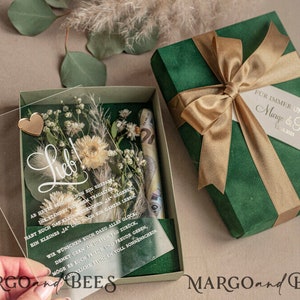May include: A green gift box with a gold ribbon and a white tag that says "For immer und ewig Margo & Robert 1. Juni 2022". The box is open and inside is a clear acrylic box with dried flowers, a gold heart, and a message that says "Lieb!"  The message continues with a poem in German.