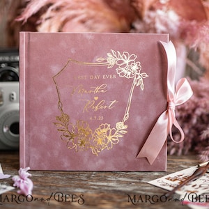 May include: A dusty rose velvet photo album with a gold foil design. The design features a floral wreath with the text "Best Day Ever" and the names "Martha Robert" with a heart and the date "4.7.23". The album is tied with a dusty rose satin ribbon.