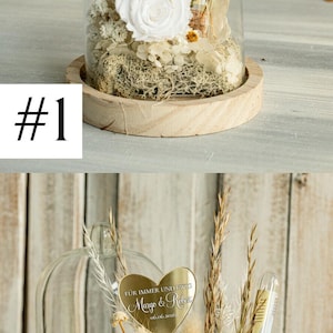 May include: A glass dome with a wooden base contains dried flowers and a gold heart-shaped plaque with the text "F&Uuml;R IMMER UND EWIG Margo & Reken 06.06.2026".
