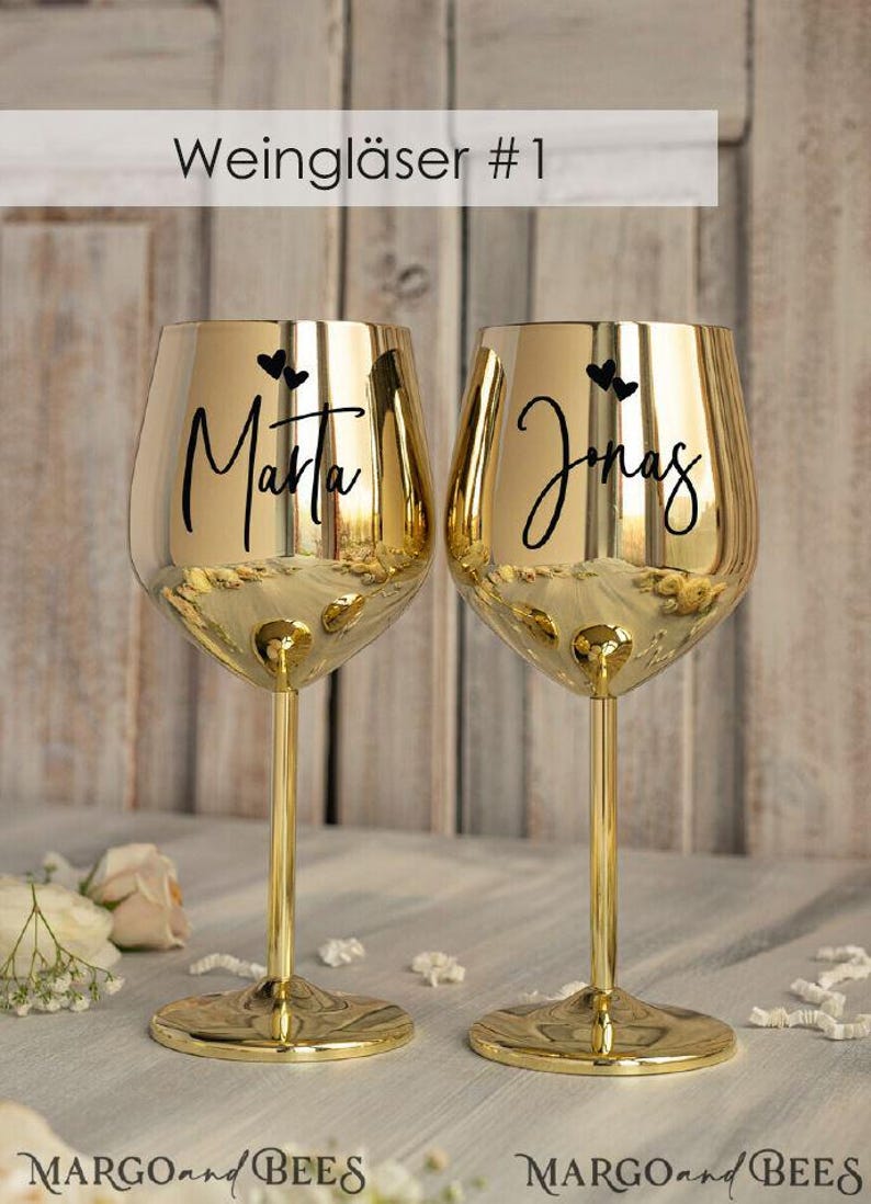 May include: Two gold-colored wine glasses with black lettering. The glasses are engraved with the names "Marta" and "Jonas" and two small hearts.
