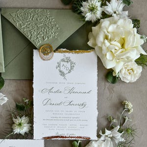May include: A white wedding invitation with deckled edges, gold foil accents, and a wax seal, featuring the text Amelia Hammond and Daniel Somersby. It is accompanied by a sage green envelope with an embossed floral pattern and white flowers.