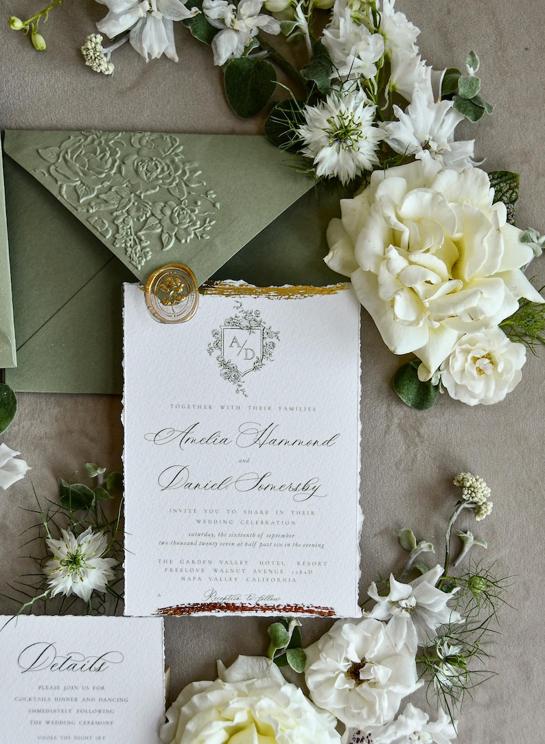 May include: A white wedding invitation with deckled edges, gold foil accents, and a wax seal, featuring the text Amelia Hammond and Daniel Somersby. It is accompanied by a sage green envelope with an embossed floral pattern and white flowers.