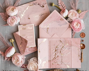 May include: Pink and gold marble wedding invitation with a clear acrylic insert. The invitation features the names "Ashley & Daniel" and the date "the 10th of October".