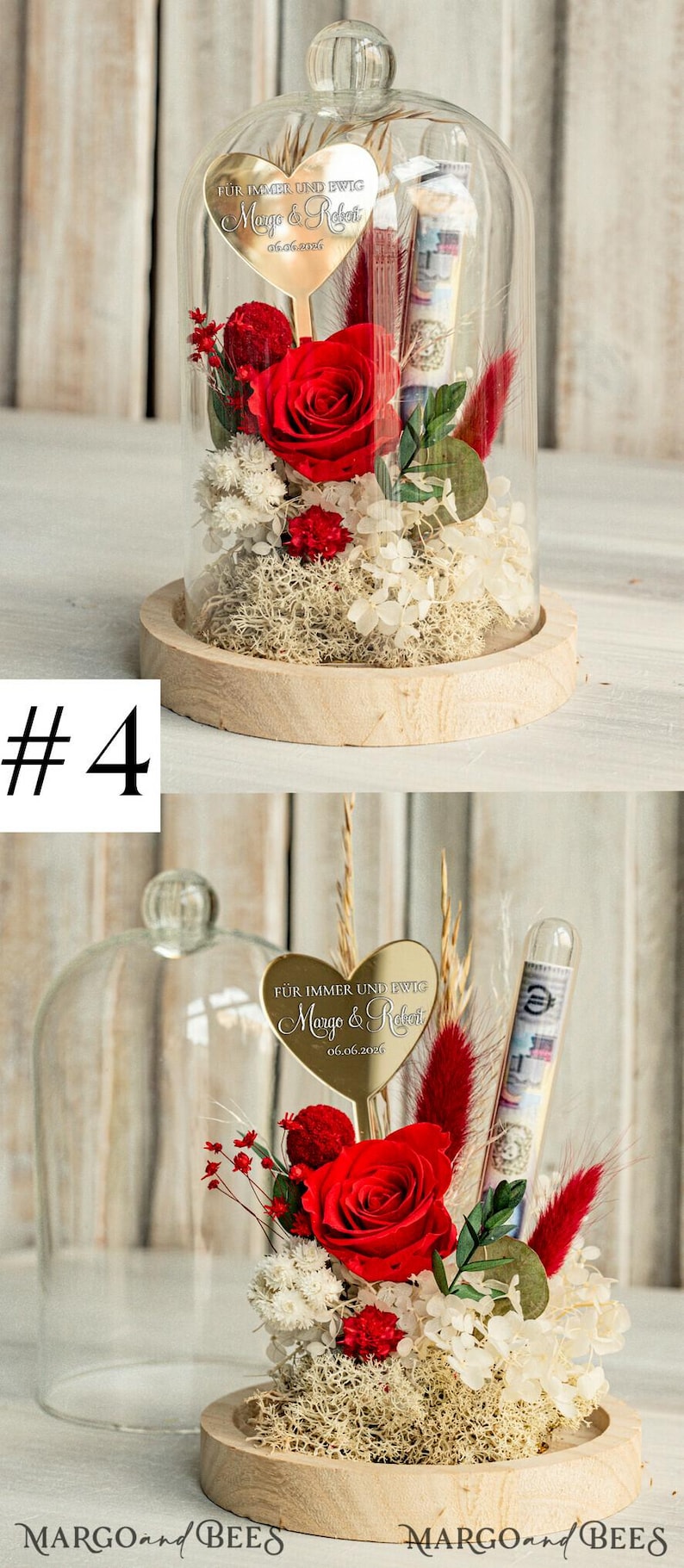 May include: A glass dome with a wooden base contains a preserved red rose, white and red dried flowers, and a gold heart-shaped plaque with the text "F&Uuml;R IMMER UND EWIG Margo & Robert 06.06.2026".