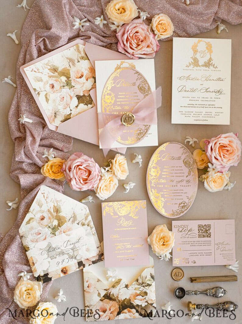 May include: Pink and gold wedding invitation suite with floral details. The invitations feature a delicate floral pattern and gold foil accents. The RSVP card has a gold foil border and the text "RSVP" in gold lettering. The invitation is set on a pink and gold fabric background with pink and yellow flowers.