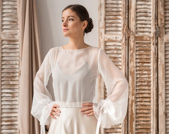 May include: A white sheer blouse with long sleeves and a gathered elastic waistband. The sleeves have ties at the wrists.