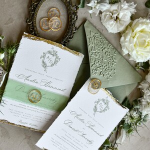 May include: Wedding invitation set featuring white textured paper with gold leaf edges, sage green belly bands, and wax seals with the initials AD. Includes a sage green envelope with a floral embossed flap and a vintage-style oval frame.