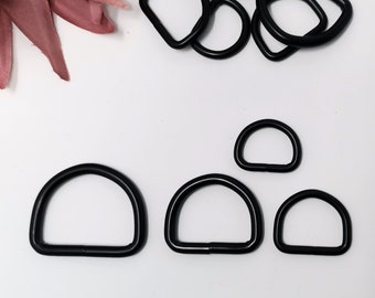 Peut inclure: Quatre anneaux en D en métal noir de différentes tailles. Les anneaux sont sur une surface blanche.