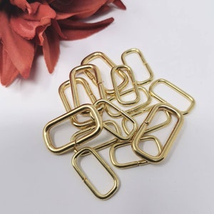Könnte beinhalten: Ein Stapel goldfarbener D-Ringe aus Metall. Die Ringe sind oval geformt und haben eine glatte Oberfläche.