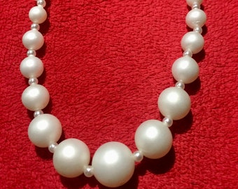 May include: A white pearl necklace with large, round pearls. The necklace is on a red background.