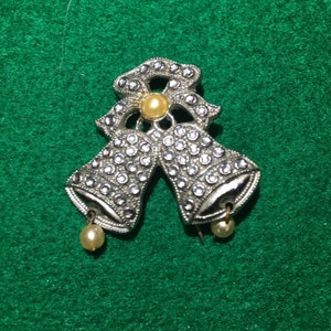 Puede incluir: Broche de campanillas de Navidad en tono plateado con un lazo y detalles de perlas.