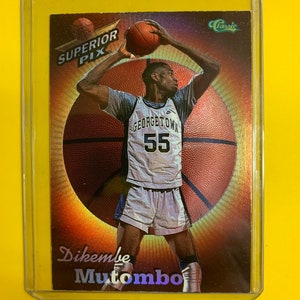 Può includere: Una carta collezionabile di basket con Dikembe Mutombo con la maglia dei Georgetown Hoyas, numero 55. La carta ha uno sfondo olografico con un design a palla da basket e il testo "Superior Pix" e "Classic".